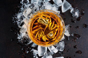 Glass of whiskey with ice cubes on black background. As whiskey is poured from the bottle into the...
