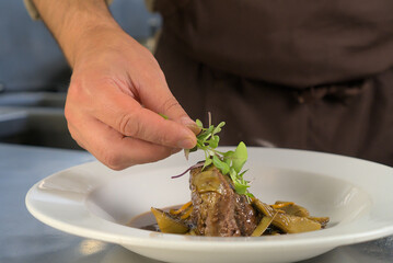 Chef carefully placing microgreens on a gourmet dish for a fine dining experience in a professional kitchen