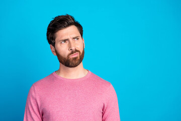 Thoughtful young man in casual wear looking curious against a vibrant blue background, considering new ideas or contemplating a decision.