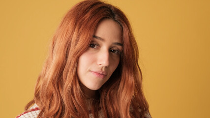 Close-up of smiling red-haired girl looking at camera in studio on yellow background