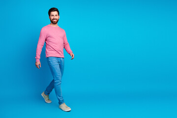 Smiling man in stylish casual attire walking confidently against a vibrant blue background, exuding...