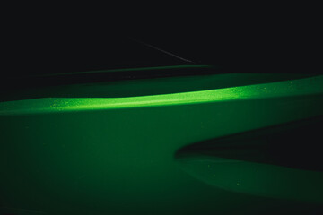 A green car with a shiny, wet paint job. The car is parked in a dark area