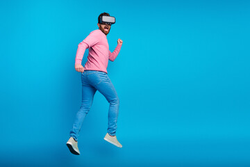Energetic man enjoying virtual reality experience with VR headset in casual outfit against vibrant blue backdrop