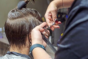 barber cuts the hair near the ears of a teenager with scissors in a beauty salon. Personal style