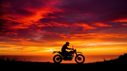 Fototapeta premium Silhouette of a motorcyclist riding on a hilltop with a fiery sunset in the background.