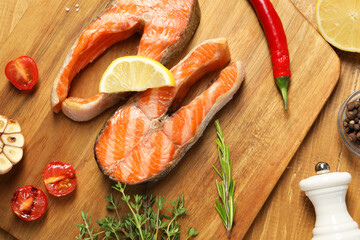 Tasty grilled salmon steaks, tomatoes, lemon and spices on wooden table, flat lay