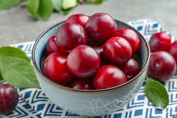 Tasty ripe plums in bowl on grey table, closeup