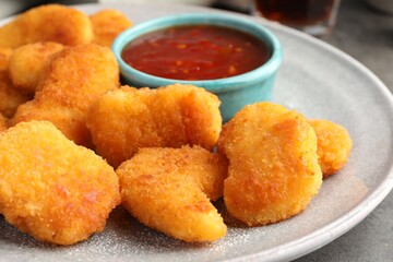 Plate with hot chili sauce and nuggets on grey table, closeup