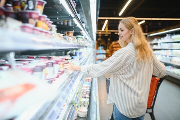 Young adult woman pushing shopping trolley between the shelves in the market