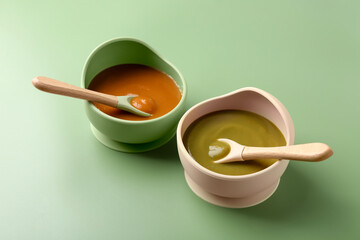 Delicious baby food with spoons in bowls on green table
