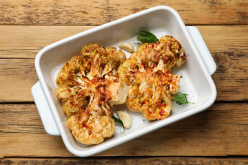 Tasty cauliflower steaks in baking dish and spices on wooden table, top view