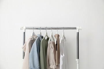 Rack with different clothes near white wall