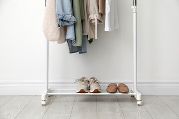 Rack with clothes and shoes near white wall
