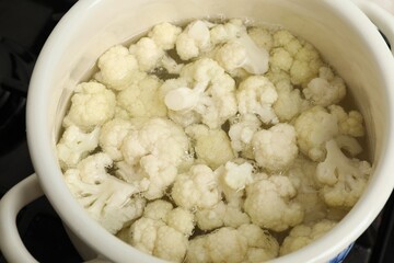 Cooking cauliflower. Florets in white pot with water on cooktop, closeup