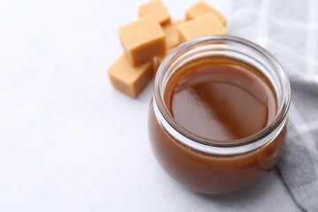 Tasty caramel sauce in jar and candies on light table, closeup. Space for text