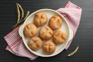 Baking dish with homemade tasty buns and spikelets on black wooden table, flat lay