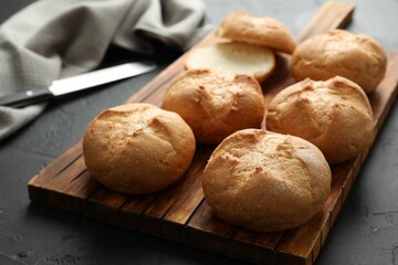 Board with homemade tasty buns on black textured table, closeup