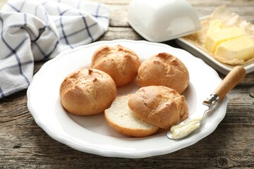 Plate with homemade tasty buns, butter and knife on wooden table, closeup
