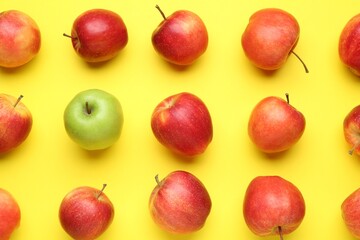 Flat lay composition with green apple surrounded by red ones on yellow background