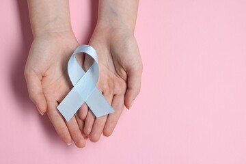 Woman with light blue ribbon on pink background, top view and space for text. Childhood cancer...