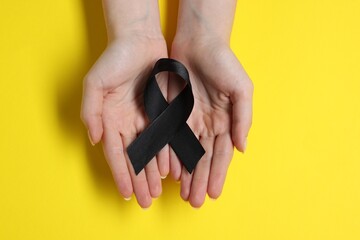 Woman with black ribbon on yellow background, top view. Melanoma and mourning concept