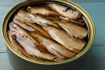 Tasty sprats in tin can on light blue wooden table, closeup