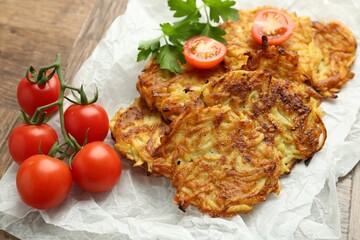 Delicious potato pancakes, tomatoes and parsley on wooden table, closeup