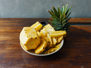 Freshly sliced pineapples displayed on a rustic wooden table with whole pineapples in the background