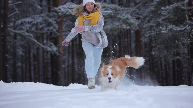 Happy girl run with border collie dog in snowy winter forest in slow motion. Merry Christmas New year Day. Cheerful puppy jump to owner. Friendship of girl and pet. Having fun together. Dogs best