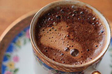 Close up a cup of Turkish coffee .Traditional Turkish Coffee. Coffee foam. Small coffee cup with blue pink floral pattern and gold detail.