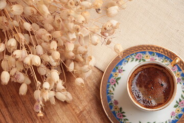 Cup of Traditional Turkish coffee with foam, dry decoration plant on the walnut wooden table and beige table cloth. Coffee foam. Coffee break time. Top view