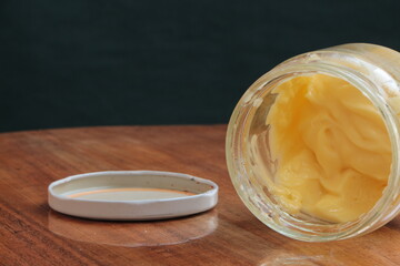 Mayonnaise sauce in glass jar. Opened mayonnaise jar and jar lid on the wooden table. Dark green background. Fresh Hommade Mayonnaise. Copy pace for text
