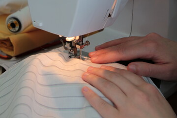 View of sewing process. Female hands stitching fabric on sewing machine at home.Hands of tailor...