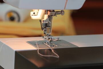 Sewing machine close up. Production line sewing machine. Needle and footstep detail. Fashion design, sewing and hobby concept. Yellow fabric and white sewing thread in the background.