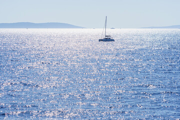 Sparkling sea in backlight with ship, island in the background, at sunset, telephoto