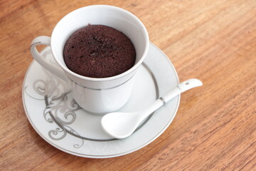 Chocolate Mug Cake. Cake in a white cup on the wooden coffee table. Chocolate cake cooked in a cup.