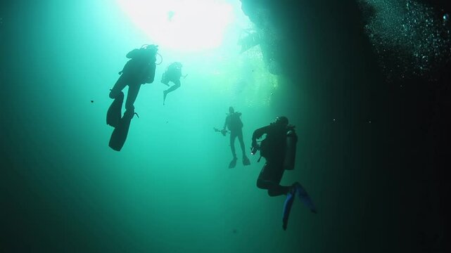 Three people are scuba diving in a dark cave. The cave is filled with water and the divers are wearing scuba gear
