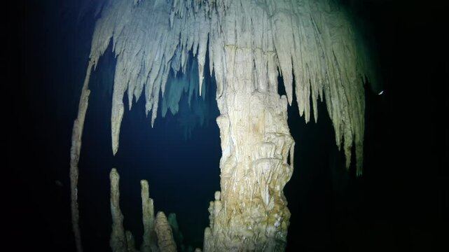 Diving deep into a mesmerizing underwater cave, showcasing stunning stalactite and stalagmite formations. A beautiful and dark exploration highlighting geological wonders illuminated by diver's lights