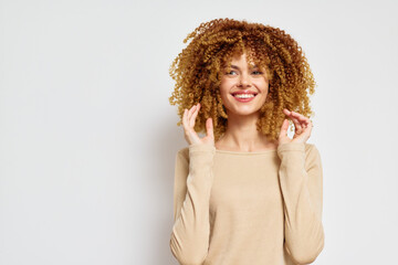 Smiling young woman with curly hair on a white background, wearing a beige top, expressing joy and confidence, ideal for beauty and lifestyle themes showcasing natural hair