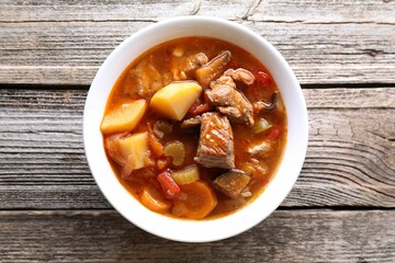 Delicious stew with vegetables in bowl on wooden table, top view