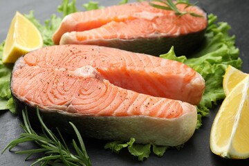 Fresh raw salmon steaks with spices, lemon, lettuce and rosemary on dark table, closeup