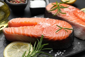 Fresh raw salmon steaks with salt, lemon and rosemary on dark table, closeup