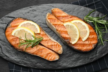 Tasty grilled salmon steaks with lemon and rosemary on dark wooden table, top view
