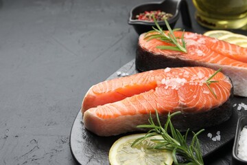 Fresh raw salmon steaks with salt, lemon and rosemary on dark textured table, closeup. Space for text