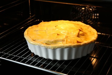 Baking dish with raw homemade apple pie in oven, closeup