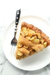 Slice of homemade apple pie and fork on white marble table, top view