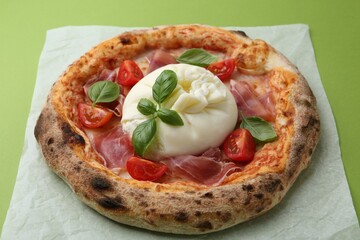 Delicious pizza with burrata cheese, basil, tomato and ham on green background, closeup