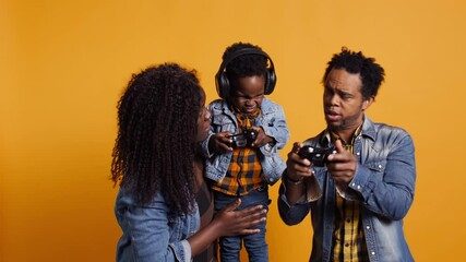 Enthusiastic father playing online video games with baby boy using controller, both parents enjoying leisure time with their small kid. African american happy family play with joystick. Camera B. - Powered by Adobe
