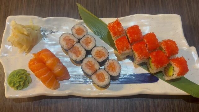 Sushi and rolls in plate. Close-up of sushi rolls on rectangle sushi plate. A set of fresh sushi rolls with salmon, avocado and black sesame seeds served on a plate with chopsticks. Japanese seafood 