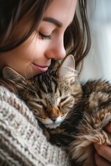 A young woman with long brown hair gently cradles a tabby cat in her arms.